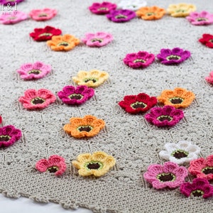 May include: A crocheted blanket with a beige background and a variety of colorful crocheted flowers in shades of pink, orange, yellow, and red.