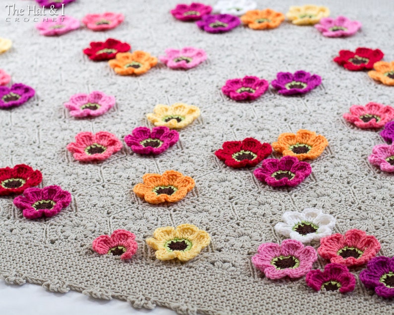 May include: A crocheted blanket with a beige background and a variety of colorful crocheted flowers in shades of pink, orange, yellow, and red.
