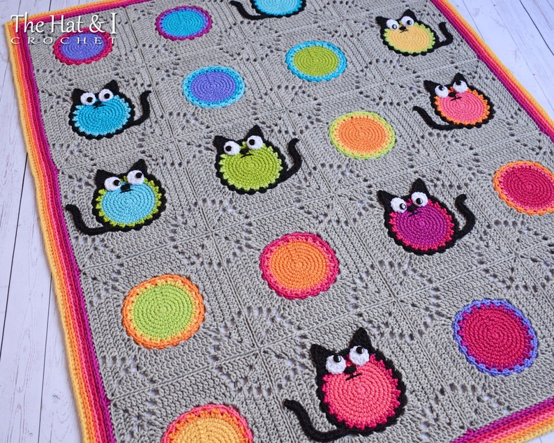 May include: A gray crochet blanket with a colorful border. The blanket features a repeating pattern of black cats with colorful bodies and circles in various colors. The text "The Hat & I Crochet" is visible in the top left corner.