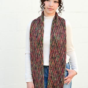 May include: A multi-colored knitted scarf and matching headband. The scarf is long and rectangular, with a textured pattern in shades of red, green, and black. The headband has a similar design. The Hat & I Crochet logo is in the top left corner.