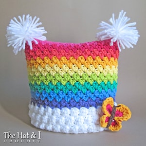 May include: A rainbow crochet hat with white pom-poms and a crocheted butterfly applique. The hat is made with a variety of colors, including red, orange, yellow, green, blue, and purple. The butterfly is brown with orange and yellow accents.