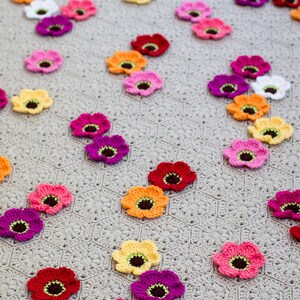 May include: A crocheted blanket with a gray background and colorful crocheted flowers in various colors, including pink, red, yellow, orange, and purple.
