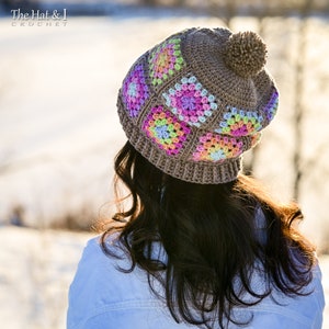 Puede incluir: Gorro de ganchillo marr&oacute;n con patrones cuadrados coloridos. El gorro tiene un pomp&oacute;n y el texto "The Hat & I Crochet". Los cuadrados coloridos incluyen tonos de rosa, amarillo, azul y verde. Accesorio de invierno.