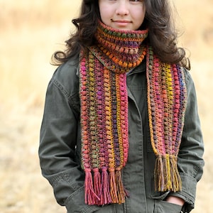 Puede incluir: Una bufanda de crochet multicolor con flecos. La bufanda est&aacute; hecha con una variedad de colores, incluyendo rojo, naranja, amarillo, verde, azul y morado. La bufanda la lleva puesta una persona con el pelo largo y casta&ntilde;o.