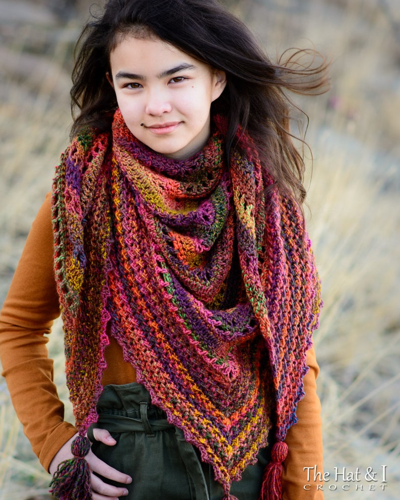 Puede incluir: Un chal de ganchillo colorido con un borde de flecos y borlas. El chal est&aacute; hecho con una variedad de colores, incluyendo rojo, naranja, amarillo, verde, azul y morado. El chal lo lleva una persona con el pelo largo y oscuro.
