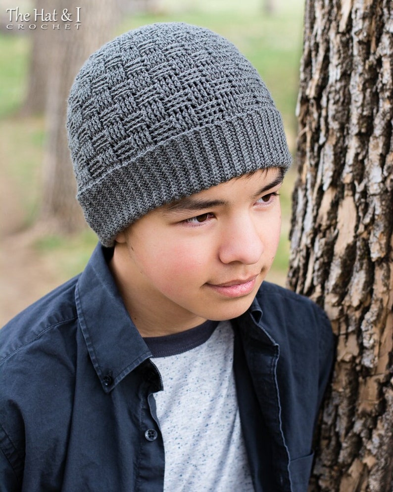 May include: A grey crocheted beanie with a textured pattern. The beanie is being worn by a person with dark hair and brown eyes.