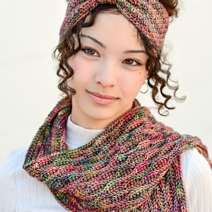 May include: A colorful, hand-knitted headband and scarf set. The headband is a knotted style, and the scarf is a cowl. The set features a mix of pink, green, yellow, and blue yarns. The text "The Hat & I Crochet" is in the top left corner.