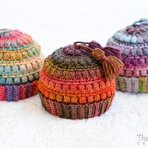 May include: Three crocheted hats with colorful yarn and tassels. The hats are made with a textured stitch and have a gradient of colors.