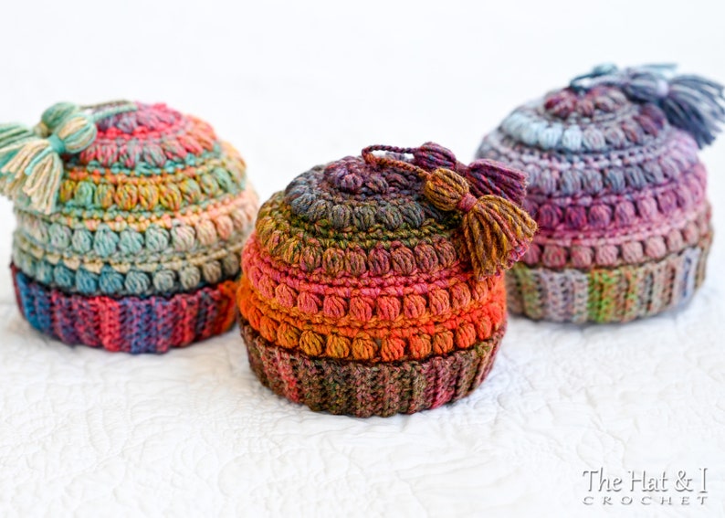 May include: Three crocheted hats with colorful yarn and tassels. The hats are made with a textured stitch and have a gradient of colors.