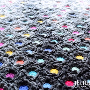 Puede incluir: Una manta de crochet gris con un degradado de color, que presenta un patr&oacute;n repetitivo de peque&ntilde;as flores de colores. Las flores est&aacute;n tejidas al crochet en varios colores, incluyendo rosa, azul, amarillo y naranja.
