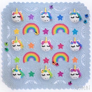 Puede incluir: Una manta de beb&eacute; de crochet con un fondo azul claro que presenta un patr&oacute;n repetitivo de arco&iacute;ris, estrellas y caras de unicornio. La manta tiene un borde festoneado.