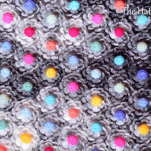 Puede incluir: Primer plano de una manta de ganchillo con un degradado de gris y blanco. La manta est&aacute; hecha de muchas peque&ntilde;as flores de ganchillo en varios colores, incluyendo rosa, azul, amarillo y verde.
