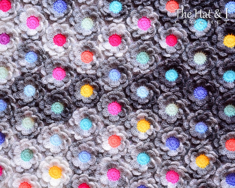 Puede incluir: Primer plano de una manta de ganchillo con un degradado de gris y blanco. La manta est&aacute; hecha de muchas peque&ntilde;as flores de ganchillo en varios colores, incluyendo rosa, azul, amarillo y verde.