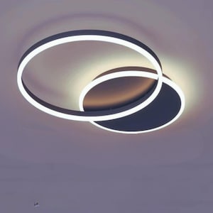 Peut inclure: Luminaire de plafond moderne avec deux formes circulaires qui se croisent. L'anneau extérieur est de couleur gris foncé, avec une bande lumineuse blanche brillante. Le cercle intérieur est gris plus foncé, avec une bande lumineuse blanche.