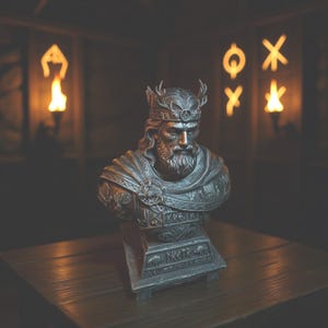 May include: A detailed bust of a king with a crown and beard, in a metallic finish. The sculpture features intricate details on the clothing and base, with inscriptions. The bust is displayed on a wooden surface, with a blurred background.