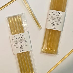 May include: Two packs of honey sticks, one with 5 sticks and the other with 10, are displayed on a white surface. The packaging includes the text "BACK PORCH BREW" and "honey sticks." The honey sticks are a golden color.