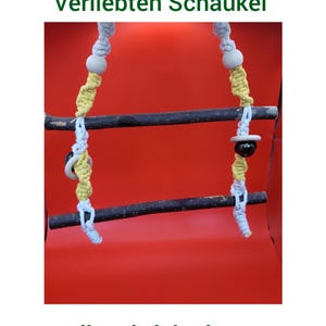 Może przedstawiać: Huśtawka dla ptaków z drewnianym drążkiem i sznurkiem makramowym w kolorze białym, żółtym i szarym. Huśtawka ma ozdobne drewniane koraliki oraz czarno-biały pierścień. U góry tekst "Verliebten Schaukel", a na dole "Wellensittich Theater".