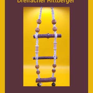 Puede incluir: Una escalera de madera artesanal para pájaros sobre un fondo amarillo. La escalera está hecha de pequeñas ramas y cuentas de madera, unidas por una cuerda blanca. El texto "Dreifacher Rittberger" y "Wellensittich Theater" se muestra en la imagen.