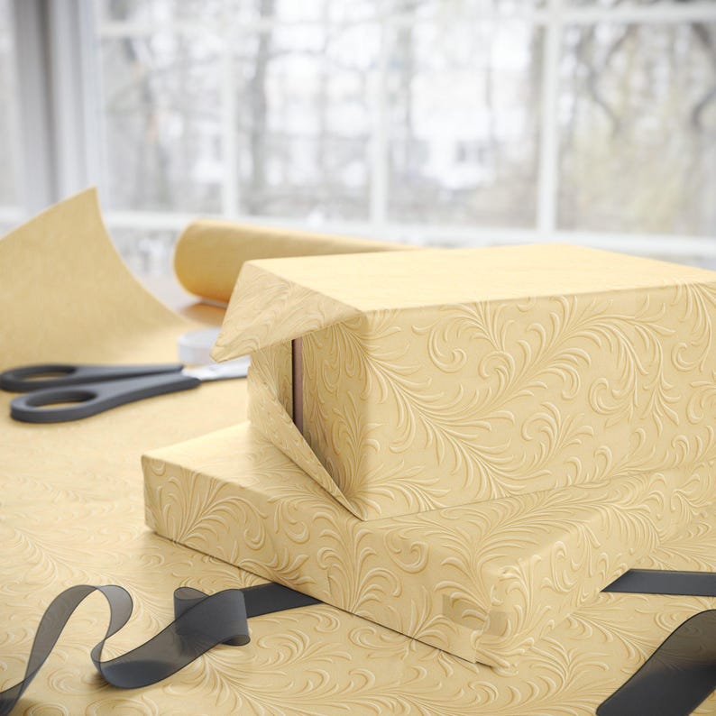 May include: Two rectangular boxes wrapped in light tan paper featuring an embossed swirling floral pattern. A roll of the same patterned paper, a pair of black scissors, and a black ribbon are positioned alongside the wrapped boxes.