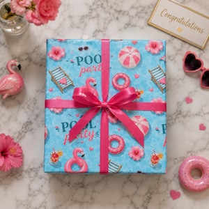 Peut inclure: Un cadeau emballé avec un motif bleu "Pool Party" avec des flamants roses, des chaises longues et des beignets. Le cadeau est noué avec un ruban rose vif. D'autres décorations roses incluent une figurine de flamant rose, des lunettes de soleil et des fleurs.