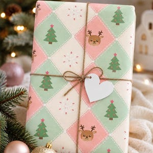 May include: A rectangular gift wrapped in paper featuring a diamond pattern with alternating pastel pink, mint green, and cream colors. The print includes small Christmas trees, snowflakes, and reindeer faces. It is tied with brown twine and a white heart tag.