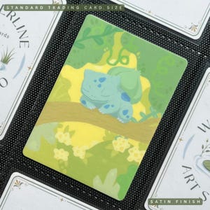 Puede incluir: Una tarjeta de tamaño estándar para coleccionables con acabado satinado que muestra a un personaje Bulbasaur de color verde claro durmiendo sobre una rama de árbol marrón. El fondo presenta un bosque soleado en amarillo brillante.