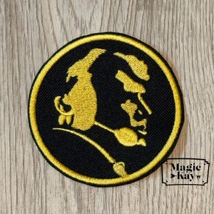 May include: Embroidered patch with a gold profile on a black circular background, edged with gold. The patch features the text "Magic Kay" in a small white rectangle in the lower right corner.