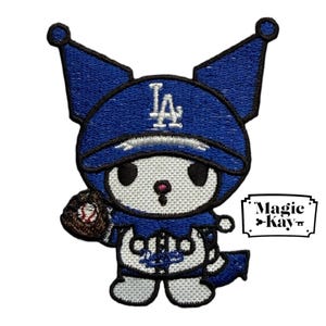 Puede incluir: Parche bordado con un personaje de dibujos animados con una gorra de béisbol azul con las letras "LA" y un guante de béisbol. El personaje es blanco con detalles negros y una nariz rosa. El parche tiene el texto "Magic Kay".