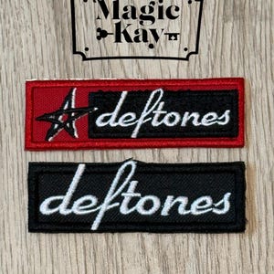 May include: Two embroidered patches with the band name "deftones" in white script. One patch is black with white text, the other is red with a black star and white text. A black and white sign above reads "Magic Kay".