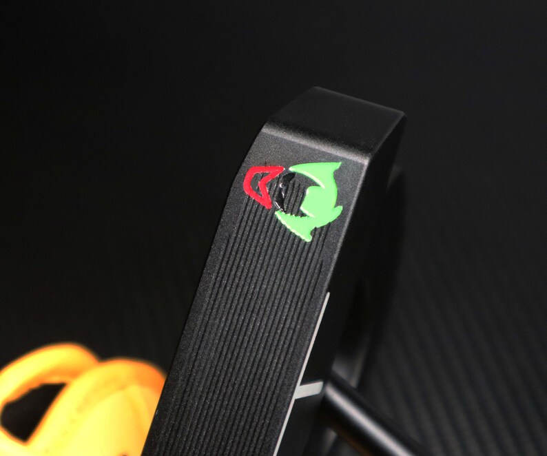 May include: A black golf putter with a textured face and a colorful logo featuring red and green accents. The putter's design includes a straight shaft and a rounded head, suitable for golf enthusiasts.