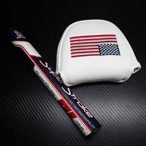 May include: A golf putter grip and head cover set. The grip is navy blue, white, and red with the text "SuperStroke". The white head cover features an embroidered American flag.