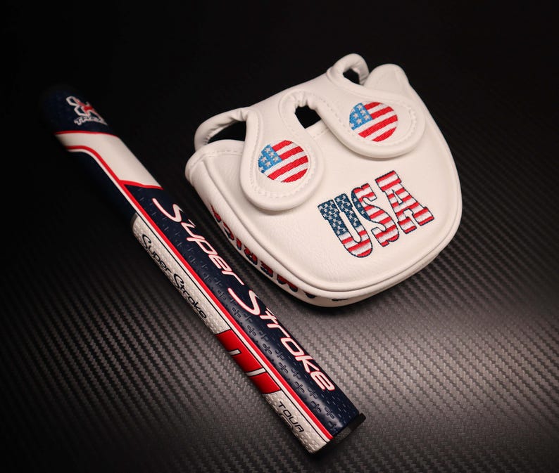 May include: A white golf putter grip and head cover set. The grip is navy blue, white, and red with the text "Super Stroke". The head cover is white with the text "USA" and American flag designs.