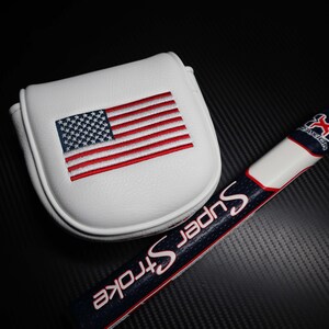 May include: White golf putter cover with an embroidered American flag in red, white, and blue. A golf club grip with the text "Super Stroke" in white and red is also visible.