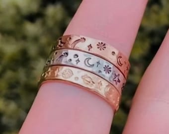 May include: Set of three gold and silver stacking rings with celestial designs, including stars, moons, and planets.