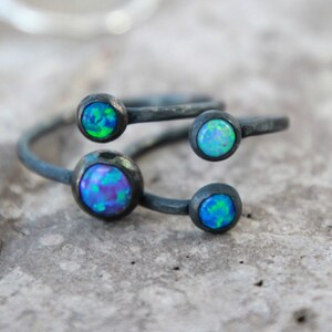 Puede incluir: Primer plano de un anillo de plata con cuatro piedras de &oacute;palo iridiscentes. El anillo tiene un dise&ntilde;o &uacute;nico con las piedras engastadas en biseles. Los &oacute;palos muestran tonos de azul, verde y morado.
