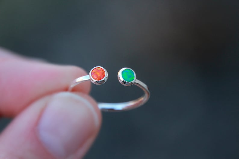 May include: A silver ring with two small round gemstones. The gemstone on the left is orange and the gemstone on the right is green.
