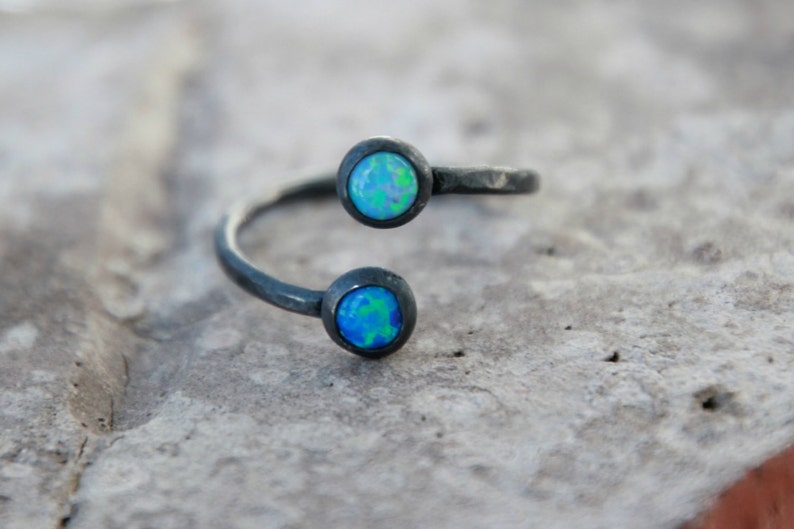 Puede incluir: Anillo plateado con dos piedras de &oacute;palo redondas engarzadas. Los &oacute;palos muestran una mezcla de tonos azules y verdes. El anillo tiene un dise&ntilde;o abierto y envolvente, y el metal tiene un acabado texturizado.