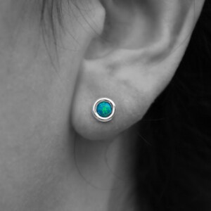 May include: A pair of silver stud earrings with a round blue opal gemstone in the center.