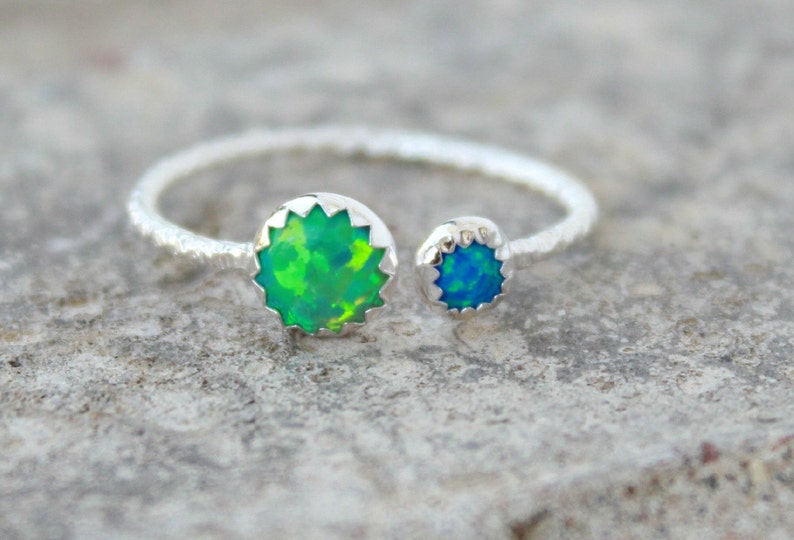 May include: A silver ring with two opal stones. The larger stone is green and the smaller stone is blue.