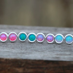 May include: A row of eight silver stud earrings with opal stones in various shades of pink and blue.