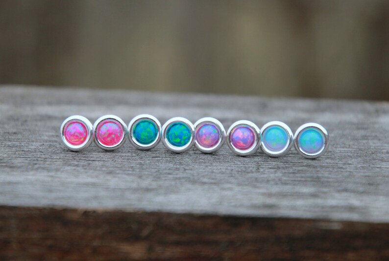 May include: A row of eight silver stud earrings with opal stones in various shades of pink and blue.