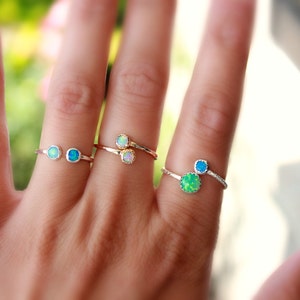 May include: Three silver rings with opal gemstones. The rings are worn on the fingers of a hand. The rings feature different colored opals, including blue, green, and white.