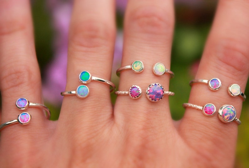 May include: A set of six silver rings with opal gemstones. The rings are designed to be worn on the middle finger and have two stones each. The opals are iridescent and come in a variety of colors, including pink, green, and blue.
