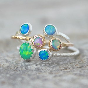 May include: A set of five silver and gold rings with opal gemstones. The rings are stacked on top of each other and feature different colored opals, including green, blue, and pink.