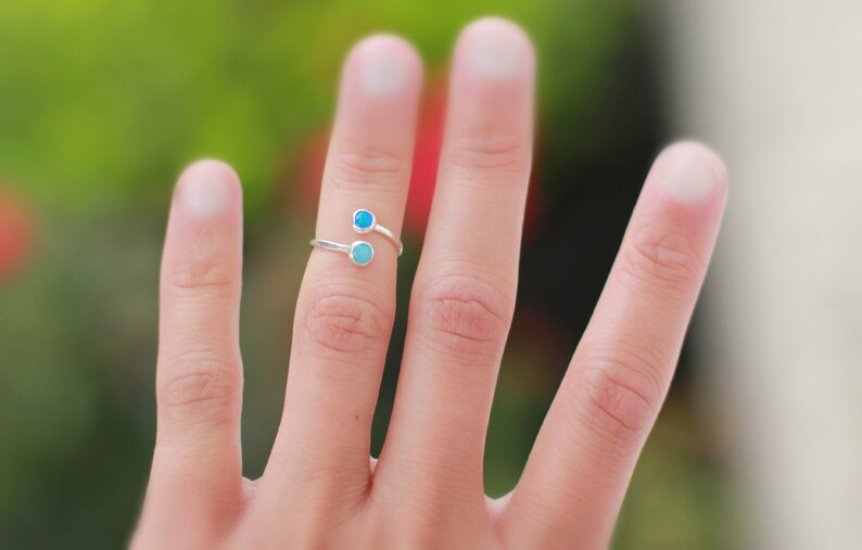 May include: A silver ring with two turquoise gemstones. The ring is worn on the middle finger of a hand.
