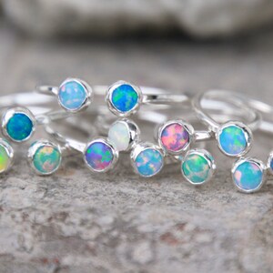 May include: A set of silver rings with opal gemstones in various colors, including blue, green, pink, and white. The rings are stacked on top of each other, showcasing the different colors of the opals.