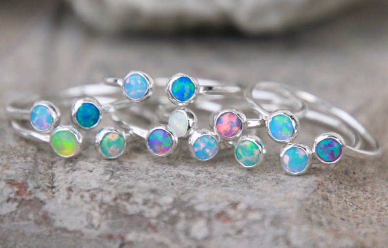 May include: A set of silver rings with opal gemstones in various colors, including blue, green, pink, and white. The rings are stacked on top of each other, showcasing the different colors of the opals.