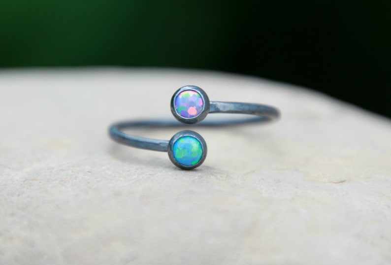 Puede incluir: Un anillo envolvente plateado con dos piedras de &oacute;palo redondas. Los &oacute;palos muestran una gama de colores, incluyendo azul, verde y rosa. El anillo est&aacute; sobre un fondo neutro.