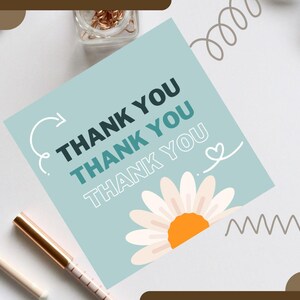 Può includere: Un biglietto azzurro con le parole "THANK YOU" ripetute, un'illustrazione di margherita e scarabocchi decorativi. Altri elementi includono un taccuino, penne, occhiali, un orologio e graffette.