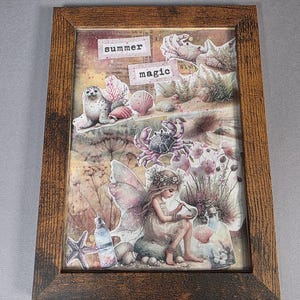 May include: A framed artwork with a summer theme. The artwork features a fairy, seashells, a seal, and the words "summer magic." The frame is brown. The artwork has a beachy, whimsical feel.